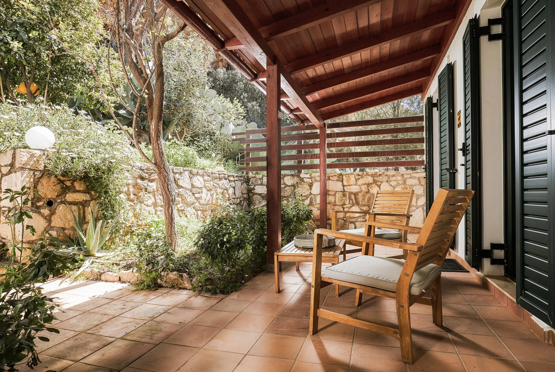 Shaded patio with wooden chairs and garden plants at Yiamas Seaside Cottage Shaded patio with wooden chairs and garden plants at Yiamas Seaside Cottage